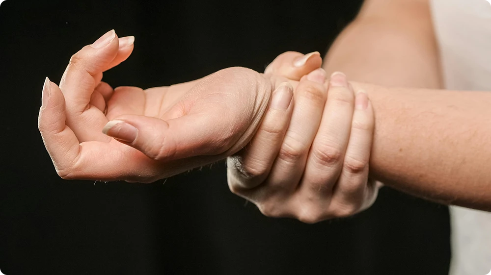 A Person holding their wrist in discomfort, suggesting a strain or injury, possibly caused by poor manual handling technique.