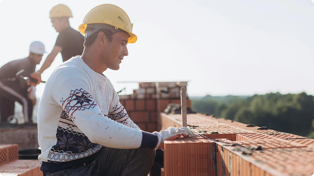 Bricklayers working on a construction site, laying bricks and applying mortar outdoors.
