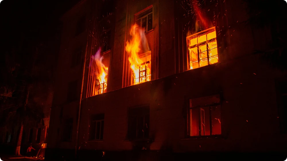 Severe building fire at night, showing flames from upper windows, highlighting fire safety risks.