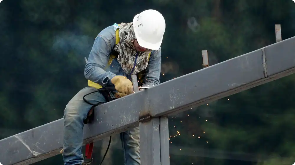 Construction worker wearing a safety harness and helmet while working on a steel frame structure at height.