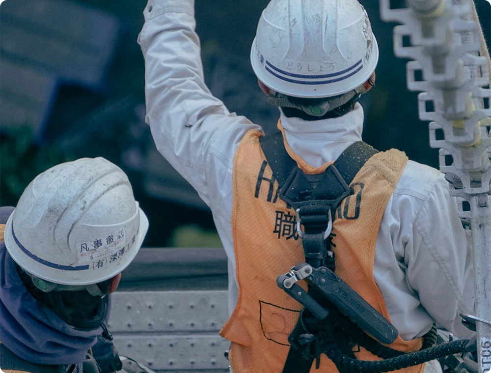 Two construction workers in safety gear and helmets communicating on a scaffolding structure at a building site, with one pointing upwards
