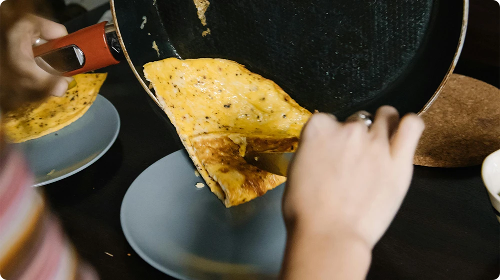 Person transferring hot food from pan to plate in a kitchen setting, highlighting the importance of cooling food before refrigeration for food safety