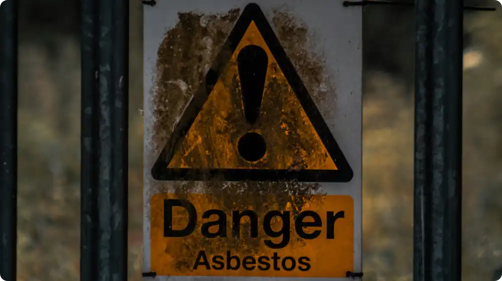 Rusty warning signs on old buildings reading Danger asbestos attached to a metal fence at a hazardous site.