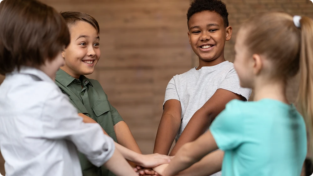 A diverse group of students placing their hands together in a show of unity and teamwork.