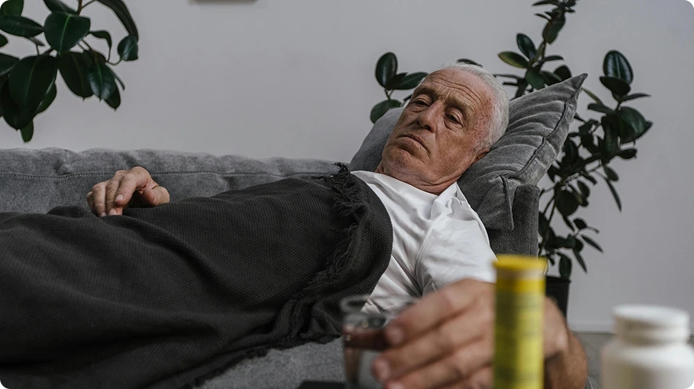 Elderly man resting on a sofa while recovering from food poisoning, with water and medicine nearby