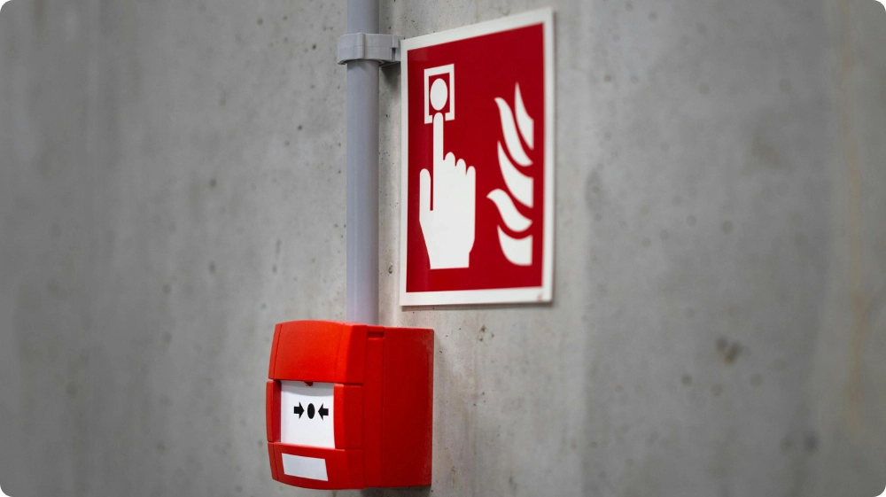 Red fire alarm sign with a hand pointing towards a fire alarm button and flames symbol.