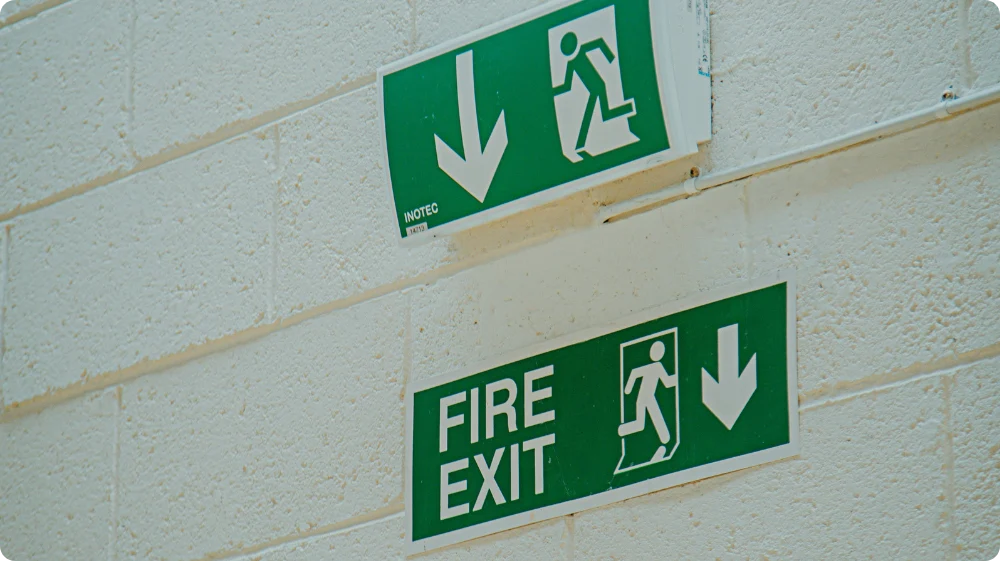 Green fire exit signs with arrows pointing downwards and a person walking towards the exit.