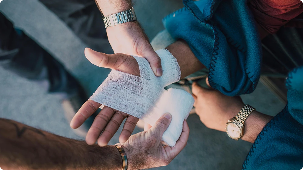  A first aid responder wrapping a roller bandage around an injured hand outdoors
