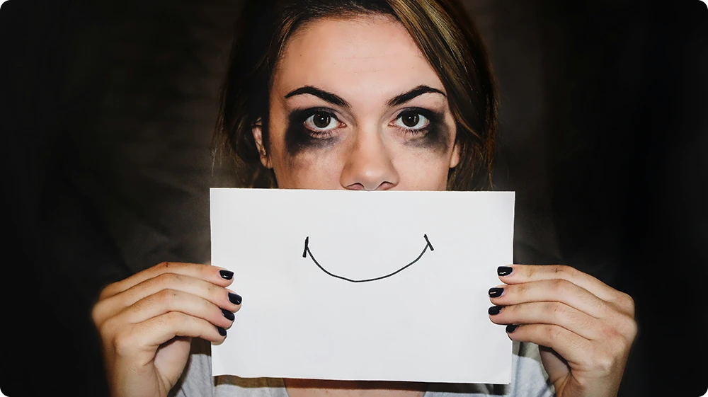 A woman hiding pain behind a smile, reflecting the impact of societal labelling