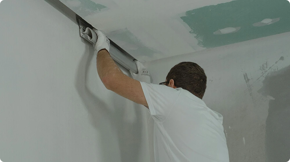 A painter smoothing a ceiling surface on-site during a painting and decorating task