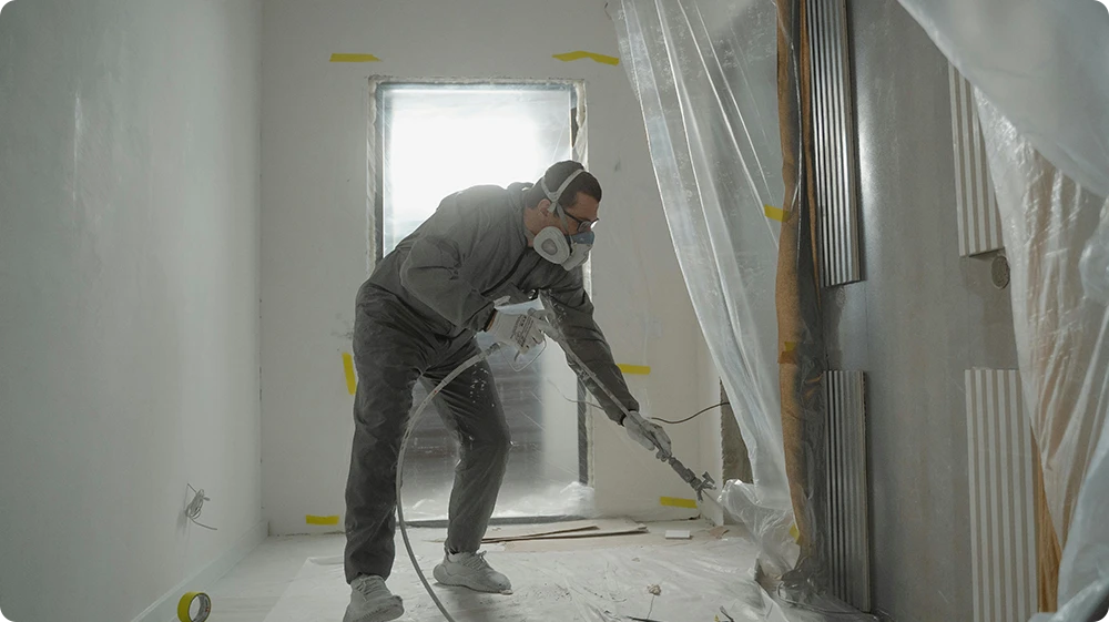 Professional painter using a spray gun to decorate an interior wall, demonstrating on-site skills for NVQ and CSCS card qualification