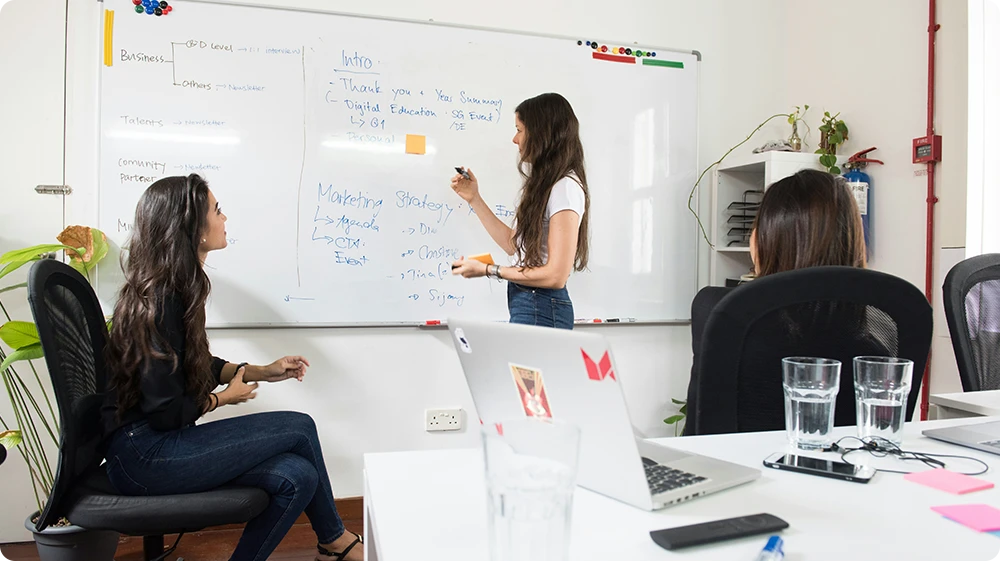 Illustration of a teacher using a digital whiteboard to explain a lesson to young students in a modern classroom setting, ideal for educational technology, digital learning, interactive teaching methods, in a primary education alongside a Teaching assistant