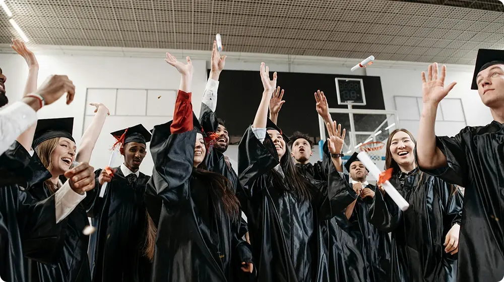 Group of university graduates in caps and gowns celebrating outside an academic building on graduation day.