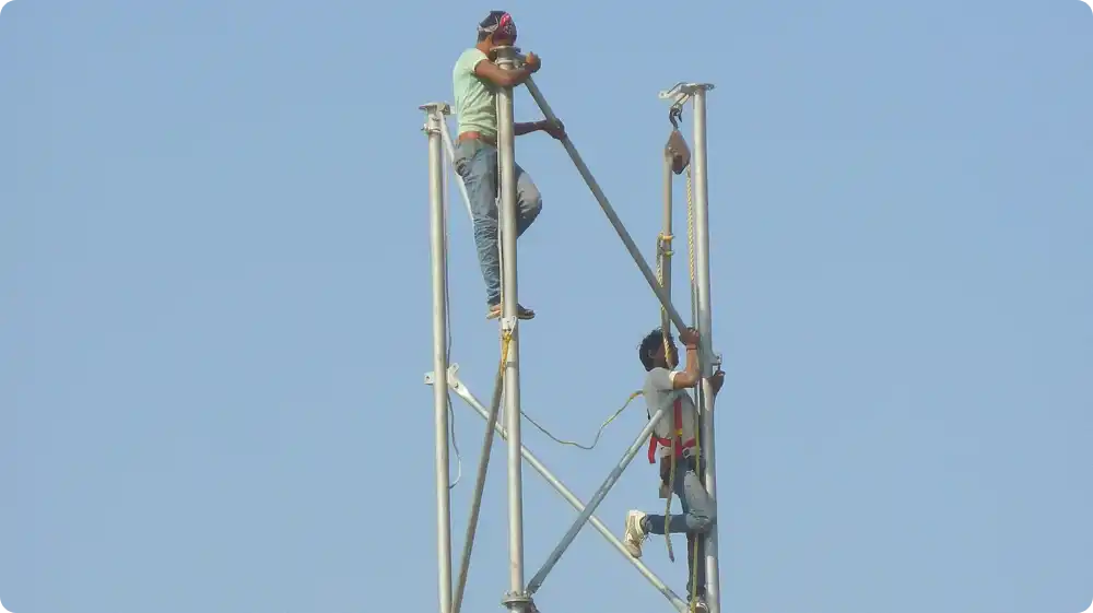 Two workers are working on a tall steel scaffold structure without proper fall protection equipment, illustrating unsafe working at height practices.