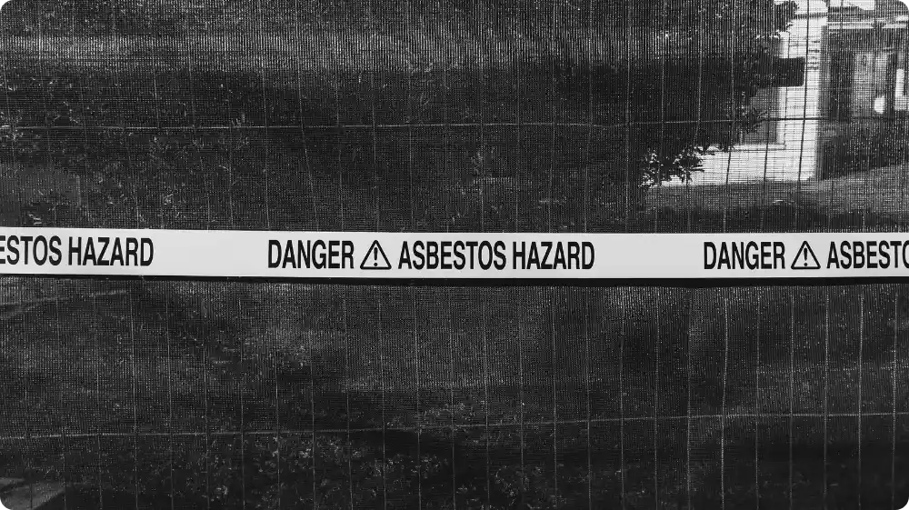 Warning tape marked Danger Asbestos Hazard placed on a fence to restrict access to the contaminated area.