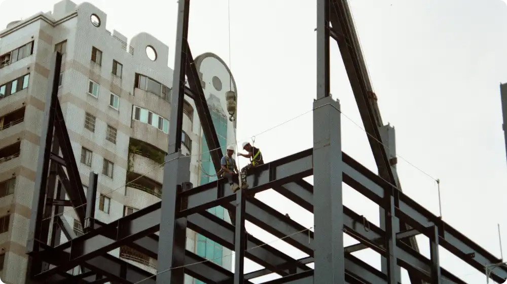 Two construction workers on a steel structure of a high-rise building, emphasising the need for safety monitoring and workload management when working at height.