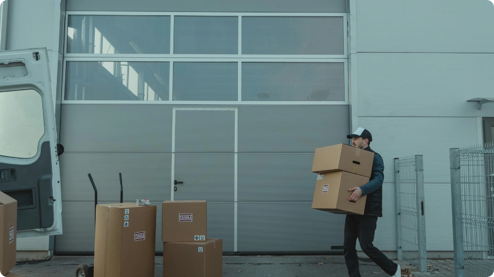 A warehouse worker is lifting a cardboard box, demonstrating proper manual handling practice.