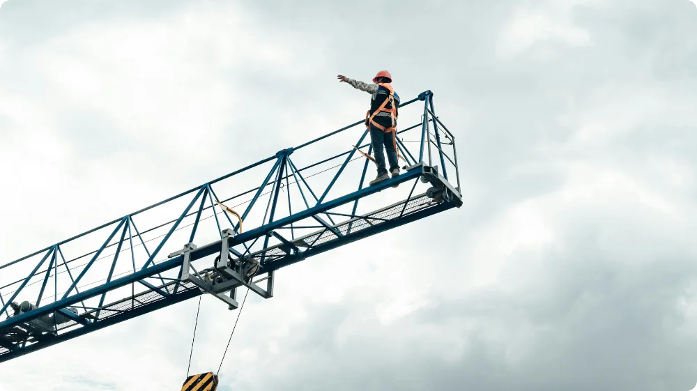 A construction worker in safety gear and a hard hat, wearing a harness and attached to a safety line while working at height.