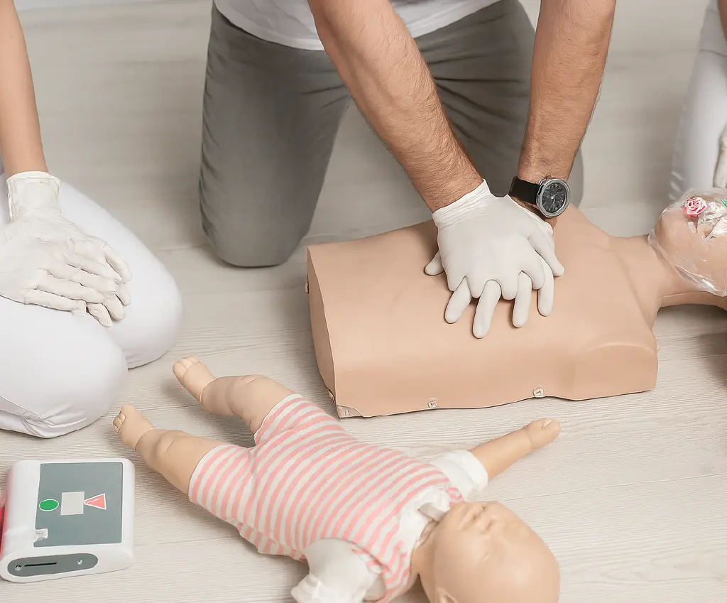 CPR practice session with mannequins for pediatric first aid training, including a defibrillator and a CPR dummy used in training for lifesaving skills